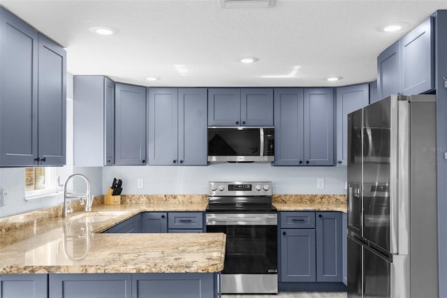 kitchen with light stone countertops, appliances with stainless steel finishes, kitchen peninsula, and sink