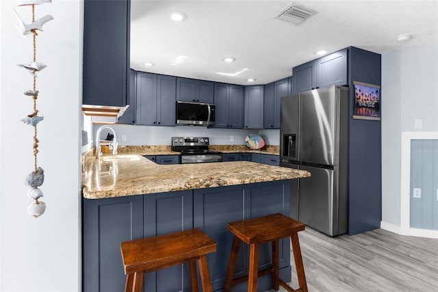 kitchen with kitchen peninsula, stainless steel appliances, hanging light fixtures, a breakfast bar, and sink