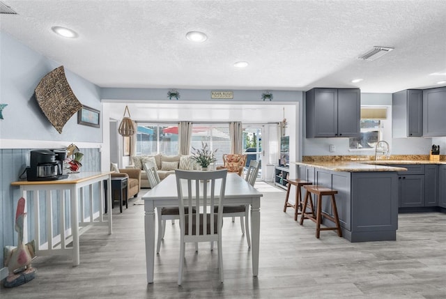 interior space with a breakfast bar area, gray cabinetry, a textured ceiling, light hardwood / wood-style flooring, and light stone counters