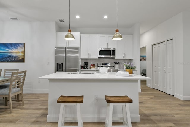 kitchen featuring stainless steel appliances, white cabinetry, tasteful backsplash, and a center island with sink