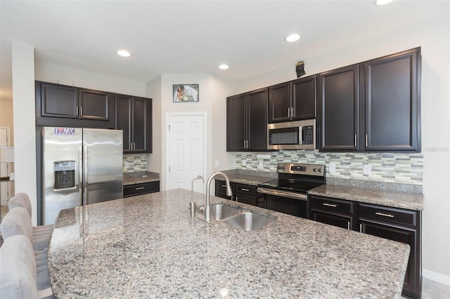 kitchen with appliances with stainless steel finishes, an island with sink, sink, decorative backsplash, and light stone counters