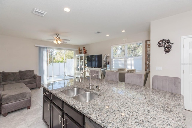 kitchen with light tile patterned flooring, sink, dark brown cabinetry, ceiling fan, and light stone countertops