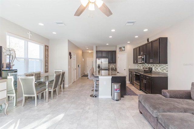 kitchen with sink, a kitchen bar, decorative backsplash, stainless steel appliances, and a center island with sink