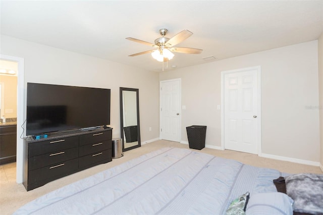 bedroom with ceiling fan, light colored carpet, and ensuite bath