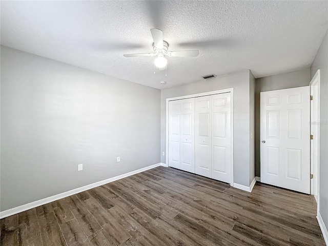 unfurnished bedroom featuring ceiling fan, a closet, dark wood-type flooring, and a textured ceiling