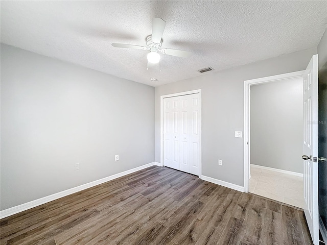 unfurnished bedroom featuring dark hardwood / wood-style flooring, ceiling fan, a closet, and a textured ceiling