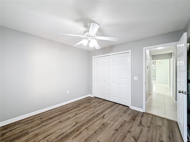 unfurnished bedroom featuring ceiling fan, a closet, wood-type flooring, and a textured ceiling