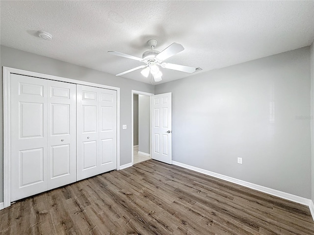 unfurnished bedroom with ceiling fan, a closet, dark wood-type flooring, and a textured ceiling