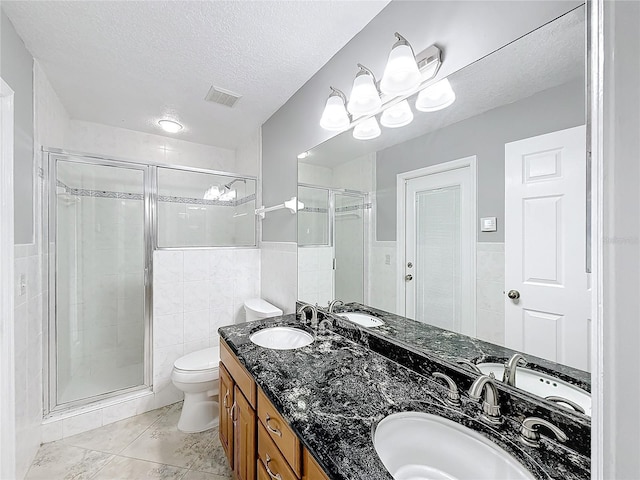 bathroom with an enclosed shower, a textured ceiling, toilet, vanity, and tile walls