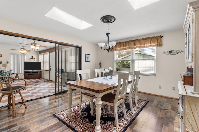 dining area with ceiling fan with notable chandelier, dark wood-type flooring, and a skylight