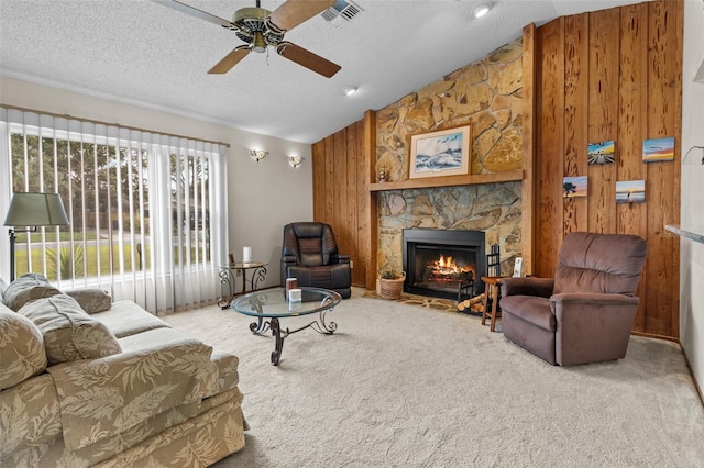 living room featuring a textured ceiling, carpet floors, a fireplace, wood walls, and ceiling fan