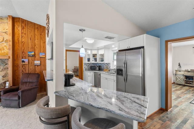 kitchen with pendant lighting, a kitchen bar, kitchen peninsula, white cabinetry, and stainless steel appliances