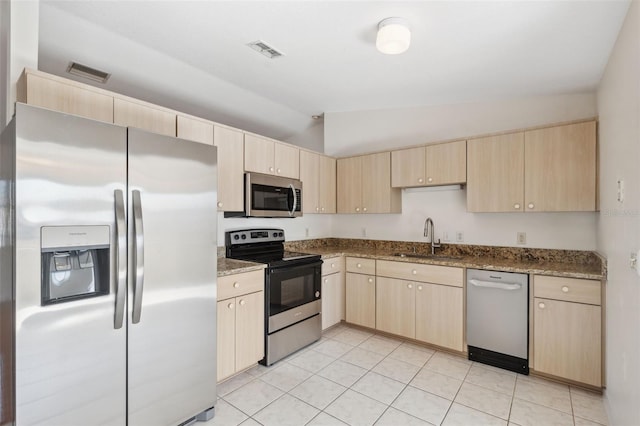 kitchen featuring stainless steel appliances, light brown cabinets, lofted ceiling, dark stone counters, and sink