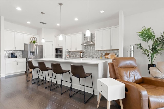 kitchen with decorative light fixtures, white cabinets, wall chimney exhaust hood, and stainless steel appliances