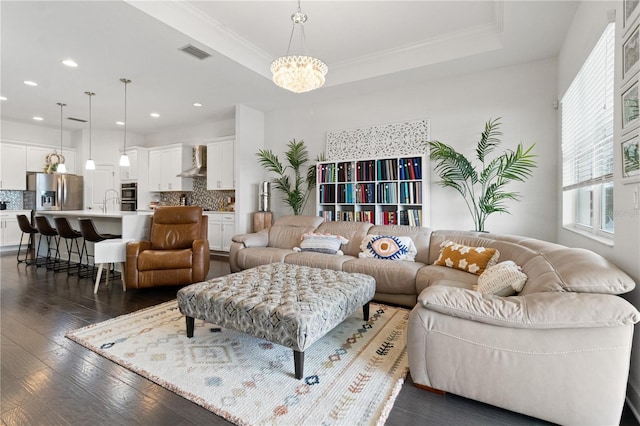 living room with a raised ceiling, sink, crown molding, dark hardwood / wood-style flooring, and a chandelier