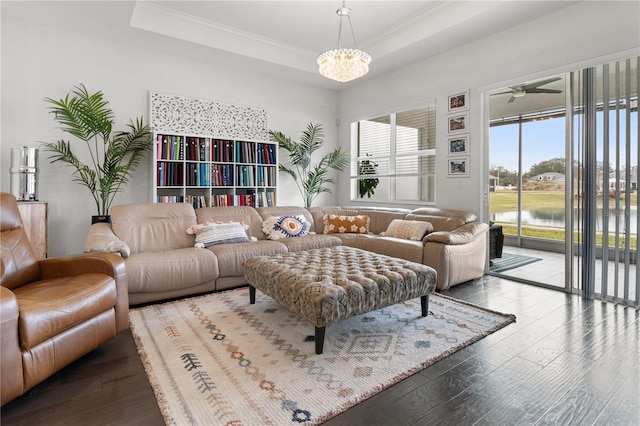 living room with crown molding, a tray ceiling, hardwood / wood-style flooring, a water view, and ceiling fan with notable chandelier