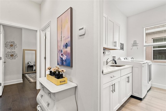 clothes washing area with washing machine and dryer, cabinets, light hardwood / wood-style flooring, and sink