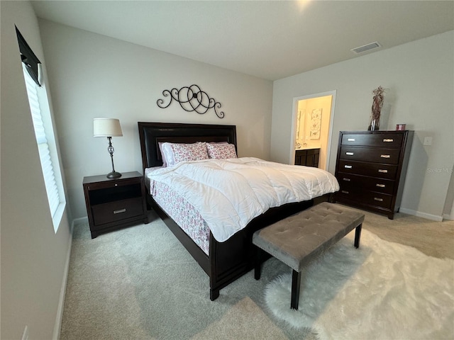 bedroom with ensuite bathroom and light colored carpet