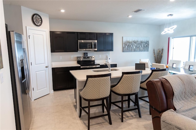 kitchen featuring stainless steel appliances, an island with sink, sink, decorative light fixtures, and light tile patterned flooring