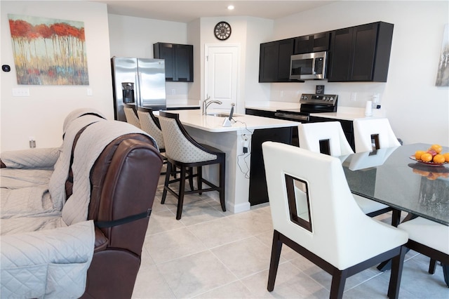 kitchen with a center island with sink, stainless steel appliances, a breakfast bar, sink, and light tile patterned flooring