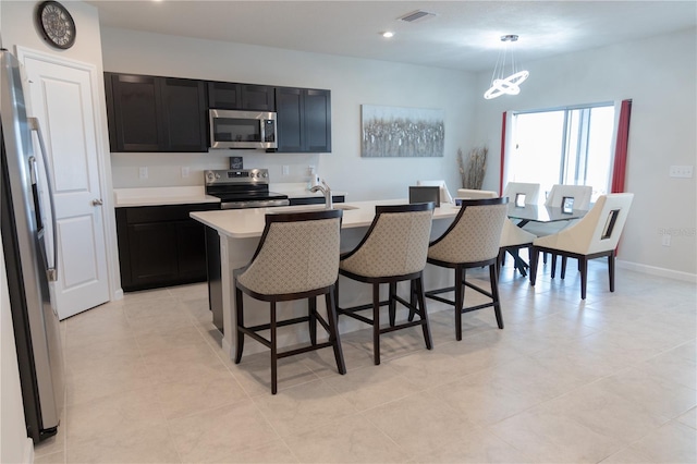 kitchen with decorative light fixtures, stainless steel appliances, a center island with sink, light tile patterned floors, and a kitchen breakfast bar