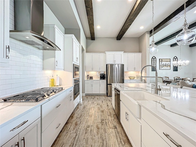 kitchen featuring hanging light fixtures, white cabinets, beam ceiling, wall chimney range hood, and stainless steel appliances