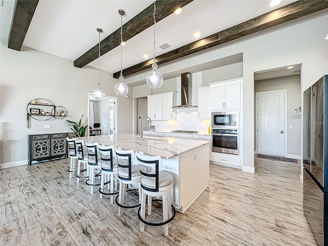 kitchen with a spacious island, white cabinetry, wall chimney range hood, sink, and stainless steel appliances