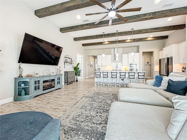 living room featuring ceiling fan, sink, beam ceiling, and light wood-type flooring