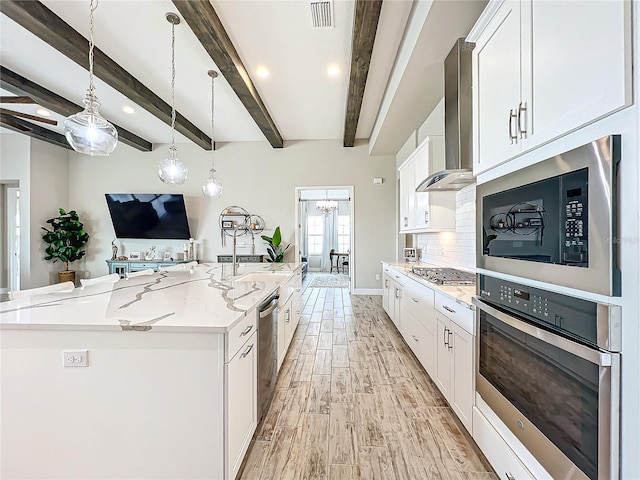 kitchen with wall chimney range hood, white cabinets, decorative light fixtures, stainless steel appliances, and a large island with sink