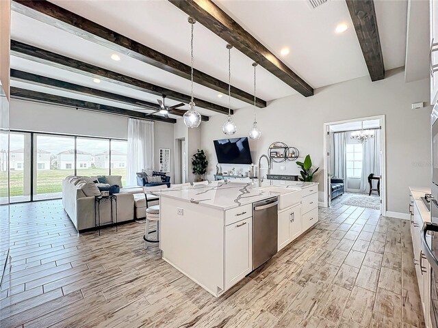 kitchen with light stone countertops, white cabinetry, hanging light fixtures, stainless steel dishwasher, and an island with sink