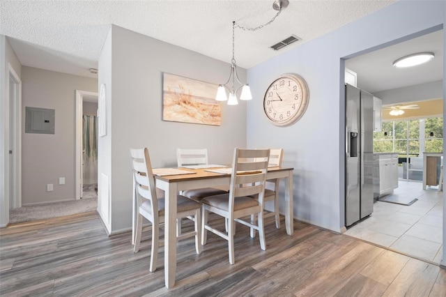 dining space with electric panel, hardwood / wood-style floors, ceiling fan with notable chandelier, and a textured ceiling