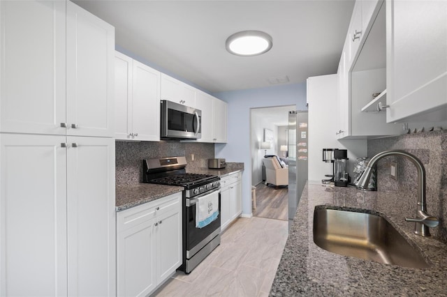 kitchen with white cabinets, stainless steel appliances, dark stone counters, and sink