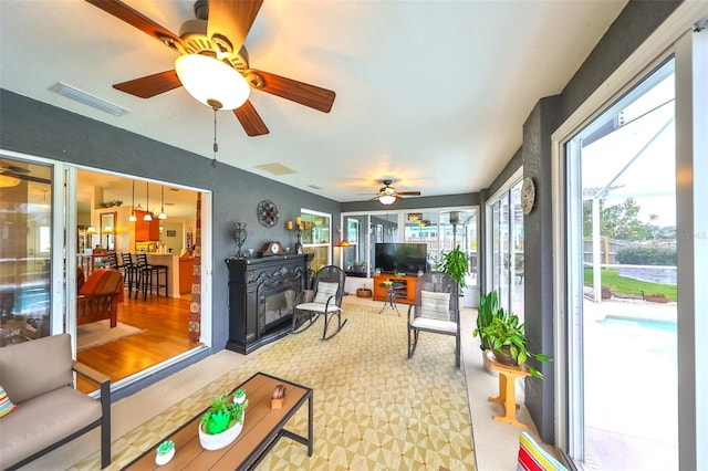 sunroom / solarium featuring visible vents, a ceiling fan, and a glass covered fireplace