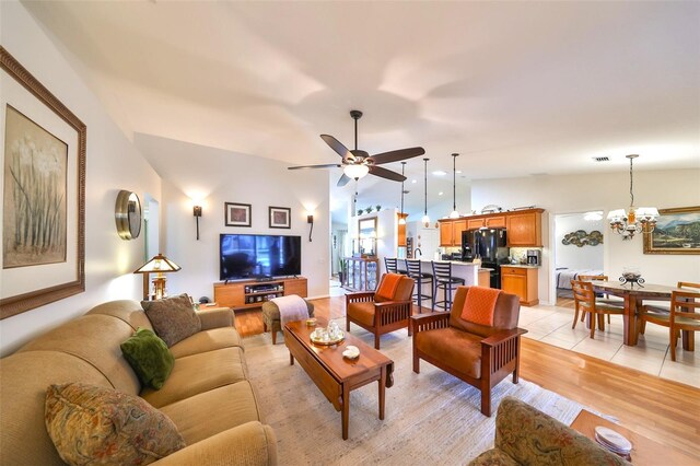 living area featuring light wood finished floors, visible vents, lofted ceiling, and ceiling fan with notable chandelier