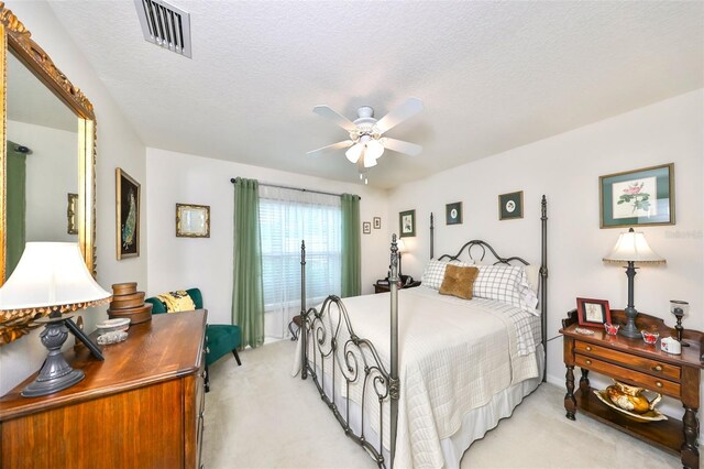 bedroom with visible vents, light colored carpet, a textured ceiling, and a ceiling fan