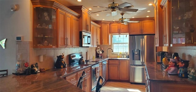 kitchen with appliances with stainless steel finishes, ceiling fan, dark stone counters, light tile patterned flooring, and tasteful backsplash