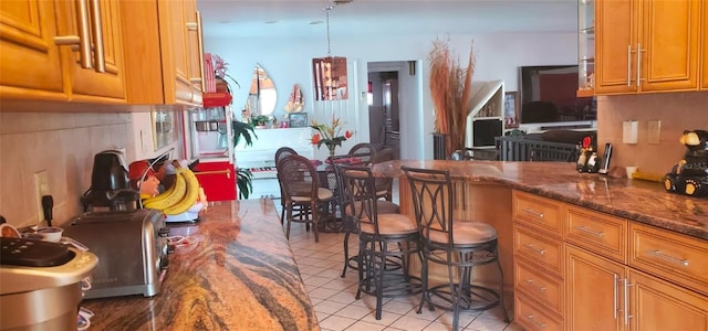 kitchen with a kitchen breakfast bar, dark stone countertops, light tile patterned floors, decorative light fixtures, and backsplash