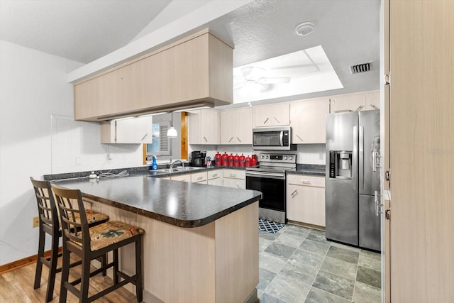 kitchen with sink, a breakfast bar area, a textured ceiling, kitchen peninsula, and stainless steel appliances