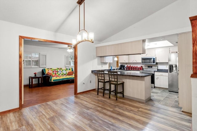 kitchen with lofted ceiling, appliances with stainless steel finishes, decorative light fixtures, a kitchen bar, and kitchen peninsula