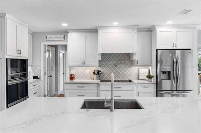 kitchen with stainless steel appliances, light stone countertops, decorative backsplash, sink, and white cabinetry