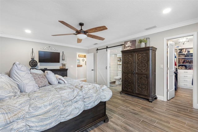 bedroom with a closet, a barn door, ceiling fan, ornamental molding, and a spacious closet