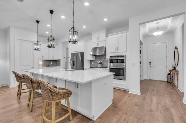 kitchen with appliances with stainless steel finishes, white cabinetry, hanging light fixtures, a large island, and backsplash