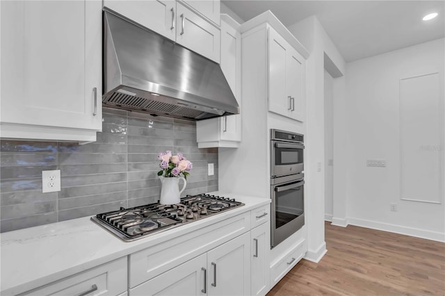 kitchen featuring light stone countertops, light hardwood / wood-style floors, appliances with stainless steel finishes, white cabinetry, and decorative backsplash