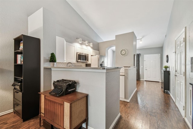 kitchen featuring stainless steel appliances, kitchen peninsula, vaulted ceiling, and white cabinets