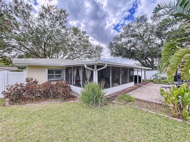 rear view of property with a sunroom, a lawn, and a patio