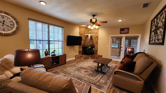 living room featuring hardwood / wood-style floors, a fireplace, ceiling fan, and a textured ceiling