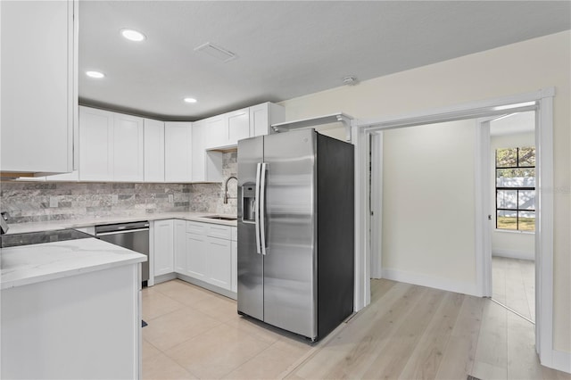 kitchen featuring sink, appliances with stainless steel finishes, white cabinetry, light stone countertops, and decorative backsplash