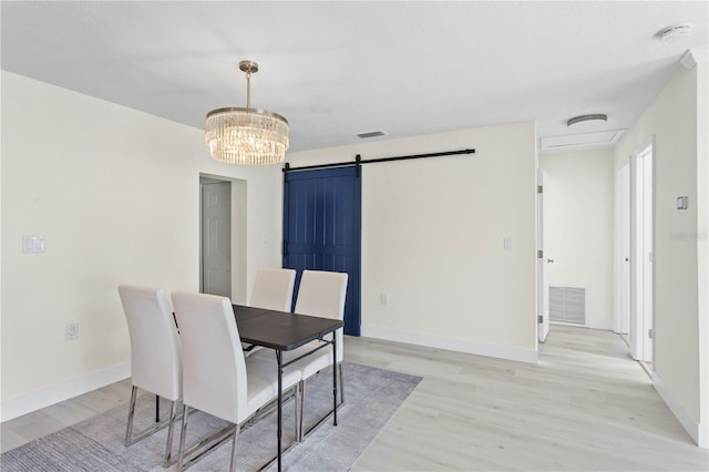 dining space with a barn door, a chandelier, and light hardwood / wood-style floors