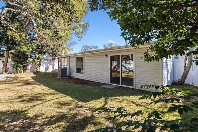 rear view of house featuring central AC unit and a yard