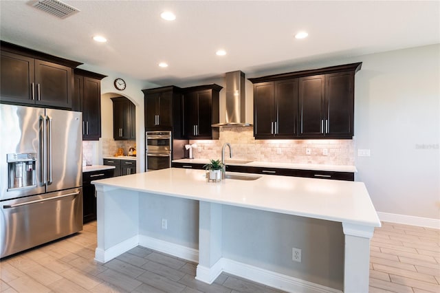 kitchen featuring sink, wall chimney exhaust hood, an island with sink, dark brown cabinets, and appliances with stainless steel finishes